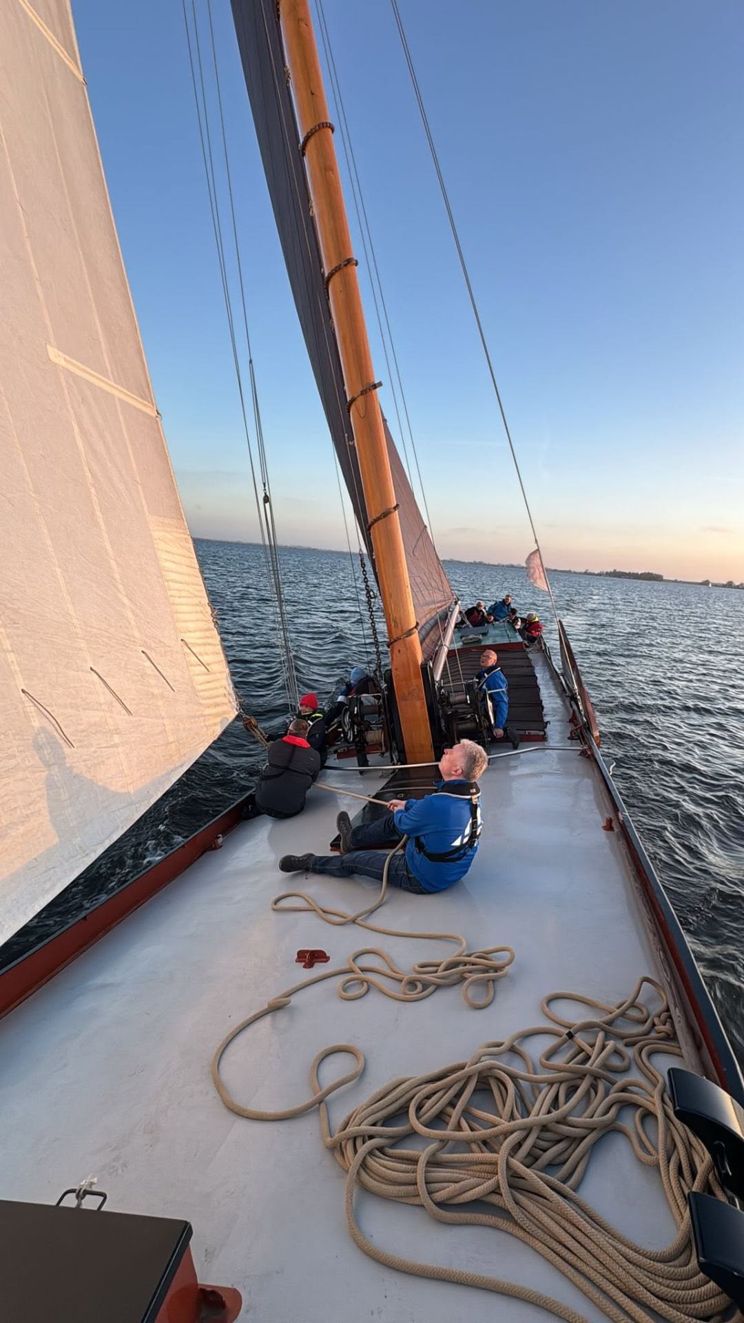 Op dek van ALE met touwwerk, mast en bemanning bij avondlicht